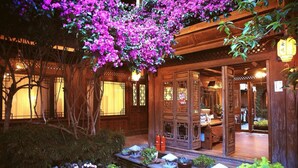 A traditional wooden building with a covered porch, potted plants, and a small garden area. - Big Tree Guesthouse (Lijiang)