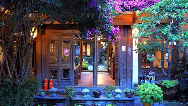 A traditional wooden house with a covered porch, potted plants, and a small garden area. - Big Tree Guesthouse (Lijiang)