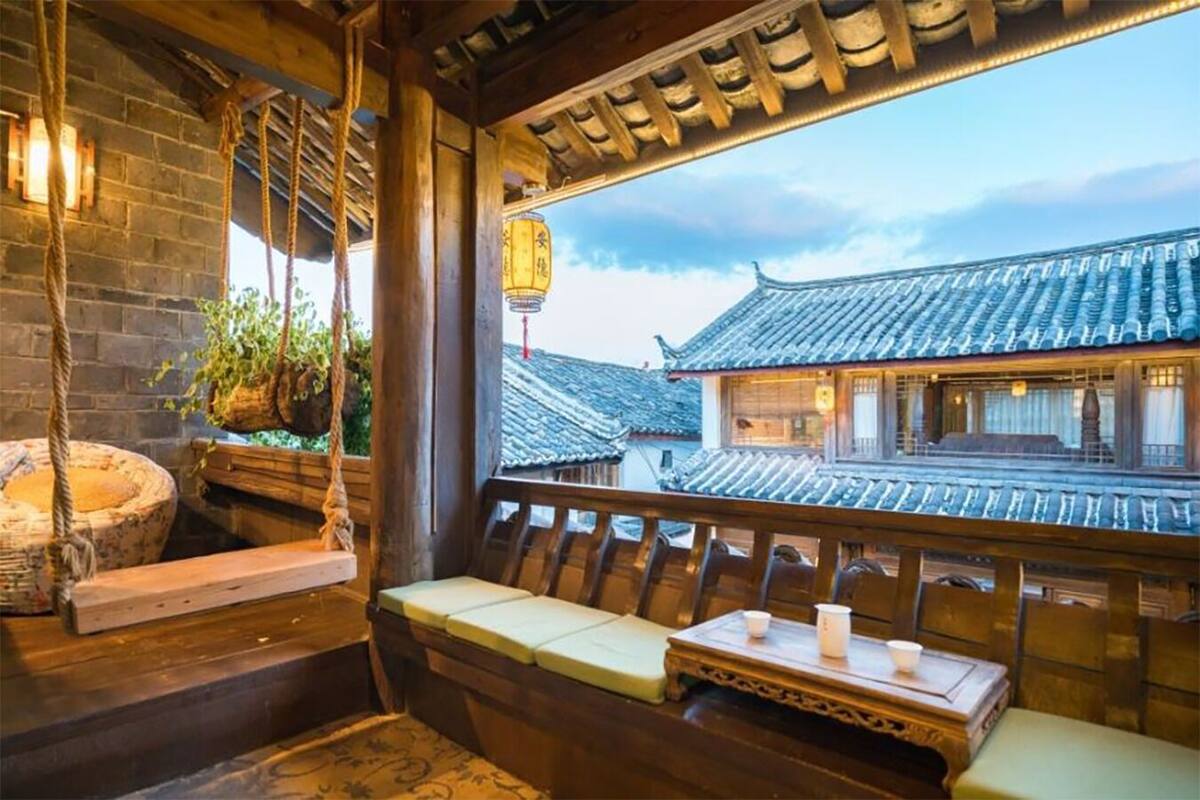 A traditional room with a wooden bench, a hanging swing, and a view of traditional buildings.