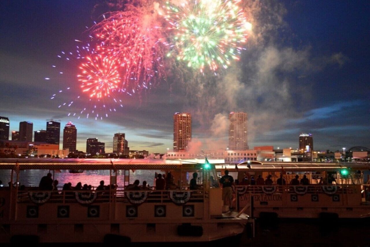 A boat with passengers enjoying a fireworks display over a city skyline.
