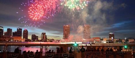 A boat with passengers enjoying a fireworks display over a city skyline.