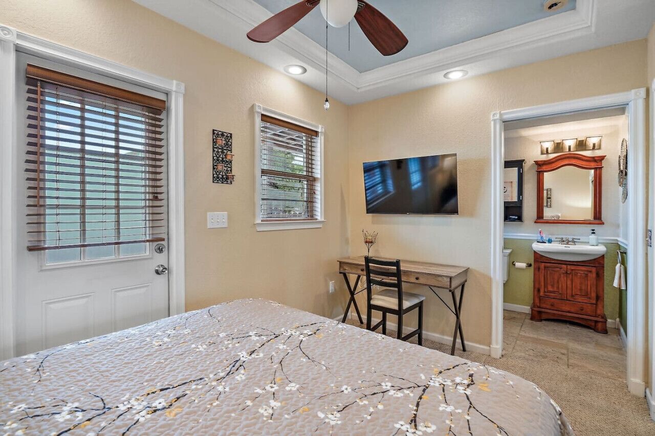 A bedroom with a bed, a desk, a chair, a TV, and a bathroom with a sink and mirror.