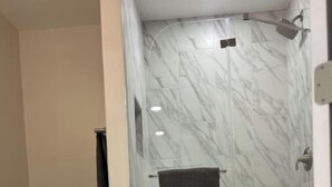 A bathroom with a toilet, a shower with a glass door, and a marble floor. - Private studio near downtown (St. Augustine)