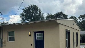 A small, single-story building with a dark blue door and windows, a light-colored exterior, and a concrete ground. - Private studio near downtown (St. Augustine)