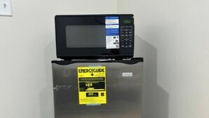 A stainless steel refrigerator with a microwave on top, an ENERGY GUIDE sticker, and a black trash bin beside it. - Private studio near downtown (St. Augustine)