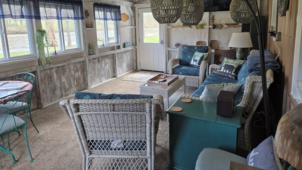A rustic interior with wicker furniture, a teal coffee table, and a dining area with a patterned tablecloth. - The Riverside Cottage... Charming  2-bedroom cottage on the Mohican River (Loudonville)