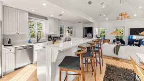 A modern kitchen with white cabinetry, a central island with bar stools, and a dining area with a sofa and coffee table.