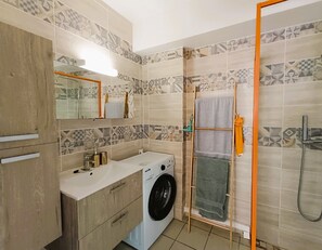 Une salle de bain moderne équipée d’un lave-linge, d’un porte-serviettes et d’une douche.