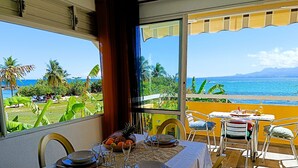A dining area with a table set for two, overlooking a scenic ocean view with palm trees and mountains. - Chez Marguerite by Magcar (Le Gosier)
