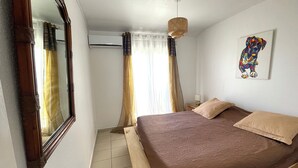 A bedroom with a bed, a mirror, a ceiling fan, and a painting on the wall. - Chez Marguerite by Magcar (Le Gosier)