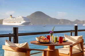 A dining table with breakfast items and a view of a cruise ship and mountains. - Oceanfront 2BR Penthouse w/ Private Jacuzzi New Year’s Week 2027 Sleeps 6 (Cabo San Lucas)