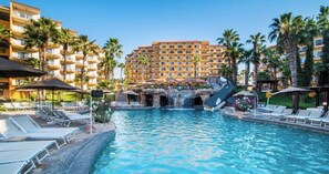 Un espace piscine d’hôtel avec des chaises longues, une cascade et des palmiers.
