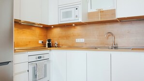 A modern kitchen with white cabinets, a wooden countertop, a built-in microwave, a coffee maker, and a stainless steel sink.