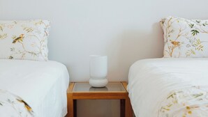 A hotel room with two beds, each with floral-patterned bedding, a bedside table with a white vase, and a plain white wall.