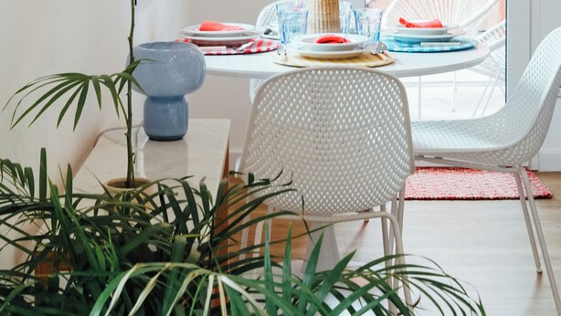 A dining area with a white table, a vase with a pink flower, and a potted plant.