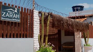 Entrada gradeada com placa indicando 'Villa Zarah', jardim de cactos e um reservatório de água.