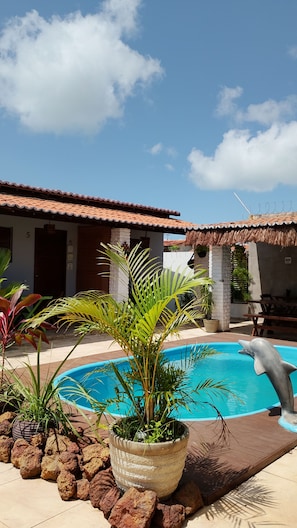Ein Pool mit einer Delfinstatue, umgeben von Kübelpflanzen und einer Terrassenanlage.