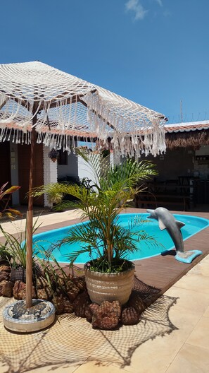 A pool area with a decorative umbrella, a potted plant, and a dolphin statue. - Pousada Villa Zarah (S ão Miguel do Gostoso)