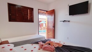 Quarto de hotel com cama, televisão, porta de madeira e vista para o exterior.