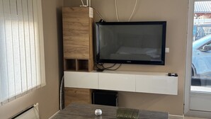 A modern living room with a flat-screen TV mounted on a white wall, a wooden cabinet, a glass coffee table with a decorative item, and a beige sofa.