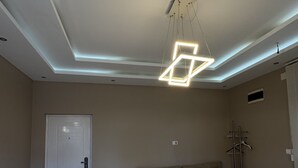 A hotel room with two single beds, a sofa, a ceiling light fixture, and a door.