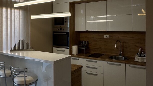 A modern kitchen with white cabinets, a wooden countertop, and a bar area with stools.