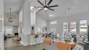 A spacious living area with a high ceiling fan, a kitchen with a bar, and large windows offering views of the outdoors. - Modern and Classy 4 Bdrm N. Scottsdale Retreat! (Scottsdale)