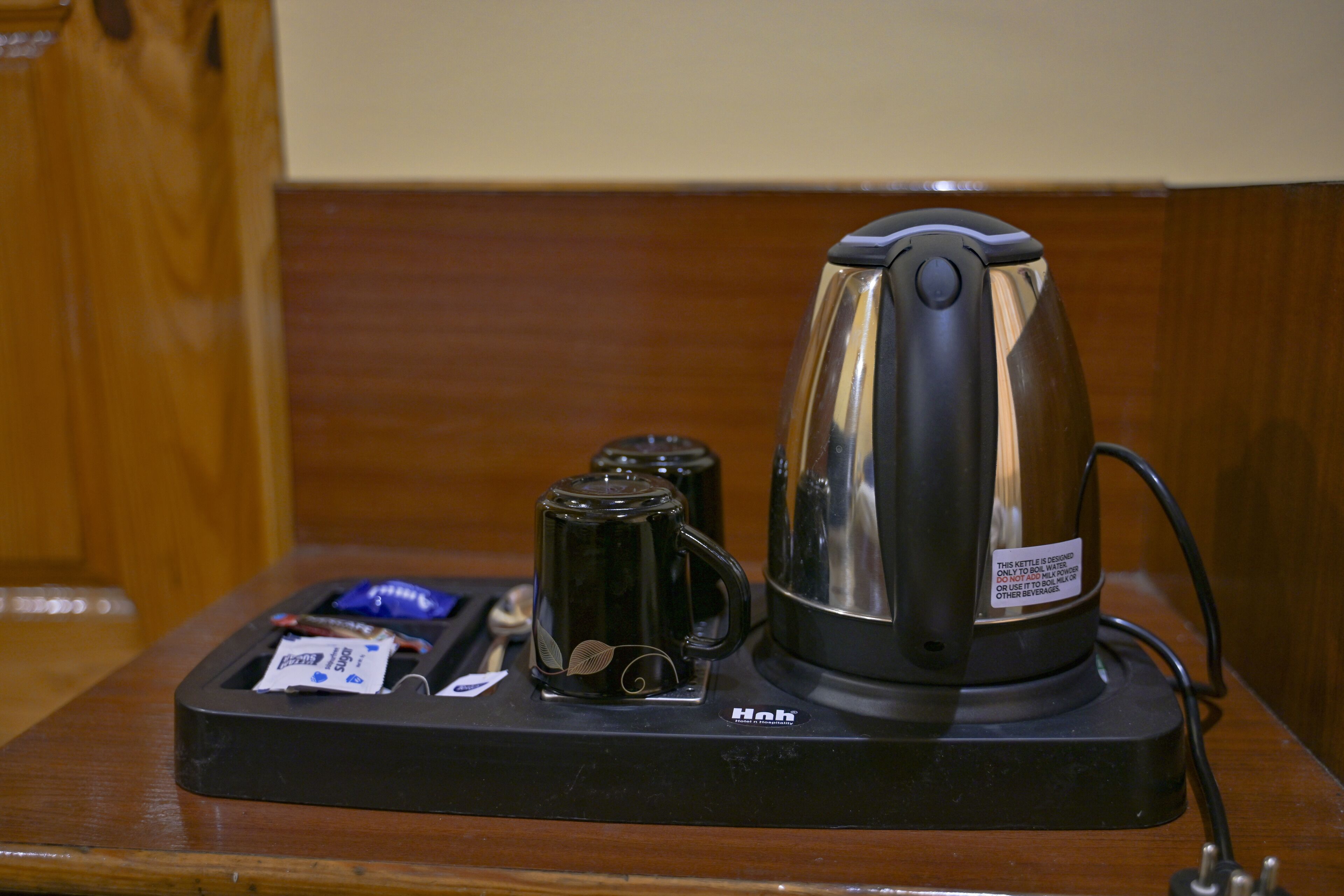 A coffee maker with a kettle on a wooden table, a tea kettle, and a packet of tea.