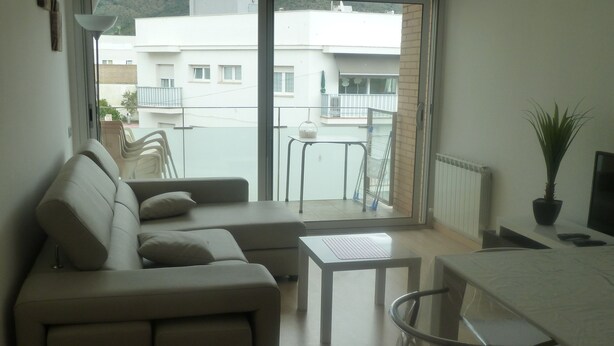 A modern living room with a sofa, a small table, and a balcony with a view of buildings. - Ten minutes from the beach, luxury apartment in the center of Rosas (Roses)