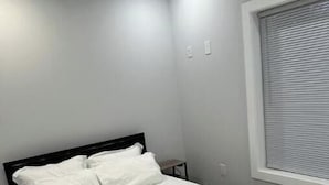 A bedroom with a bed, a window with blinds, and a light switch on the wall.
