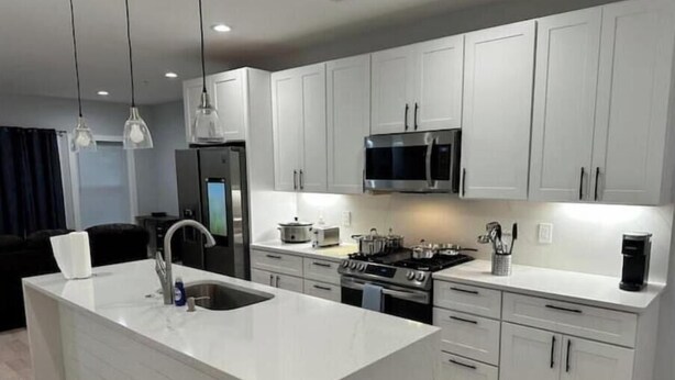 A modern kitchen with white cabinetry, stainless steel appliances, and pendant lighting.