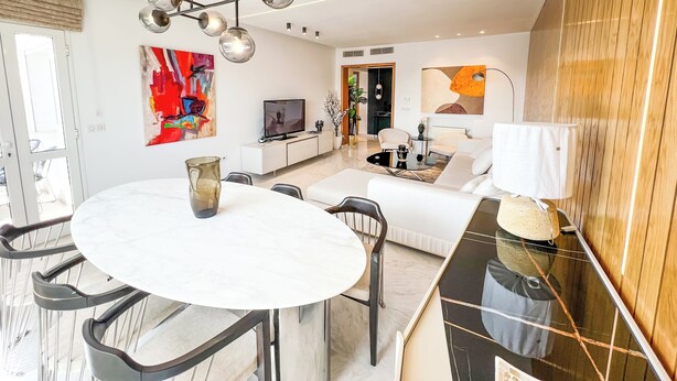 A modern living room with a white sofa, a dining table with chairs, a TV, and abstract art on the walls. - Paradis Citadin (La Marsa)
