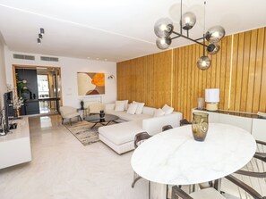 A modern living room with a white sofa, a round dining table, and a wooden accent wall. - Paradis Citadin (La Marsa)