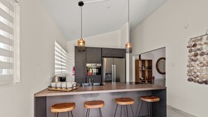 A modern kitchen with a central island, bar stools, pendant lighting, and a decorative shell wall. - Kas di Rosa, 8p luxury villa, private pool, large outdoor area (Grote Berg)
