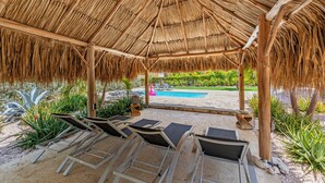A covered outdoor area with lounge chairs and a pool in the background. - Kas di Rosa, 8p luxury villa, private pool, large outdoor area (Grote Berg)
