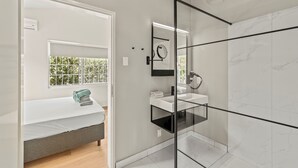 A modern bathroom with a glass-enclosed shower, a white sink, and a bed with a view of greenery outside. - Kas di Rosa, 8p luxury villa, private pool, large outdoor area (Grote Berg)