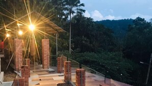 A rooftop terrace with brick pillars, a glass railing, and a view of a forested hillside. - Sankara Garden (Seremban)