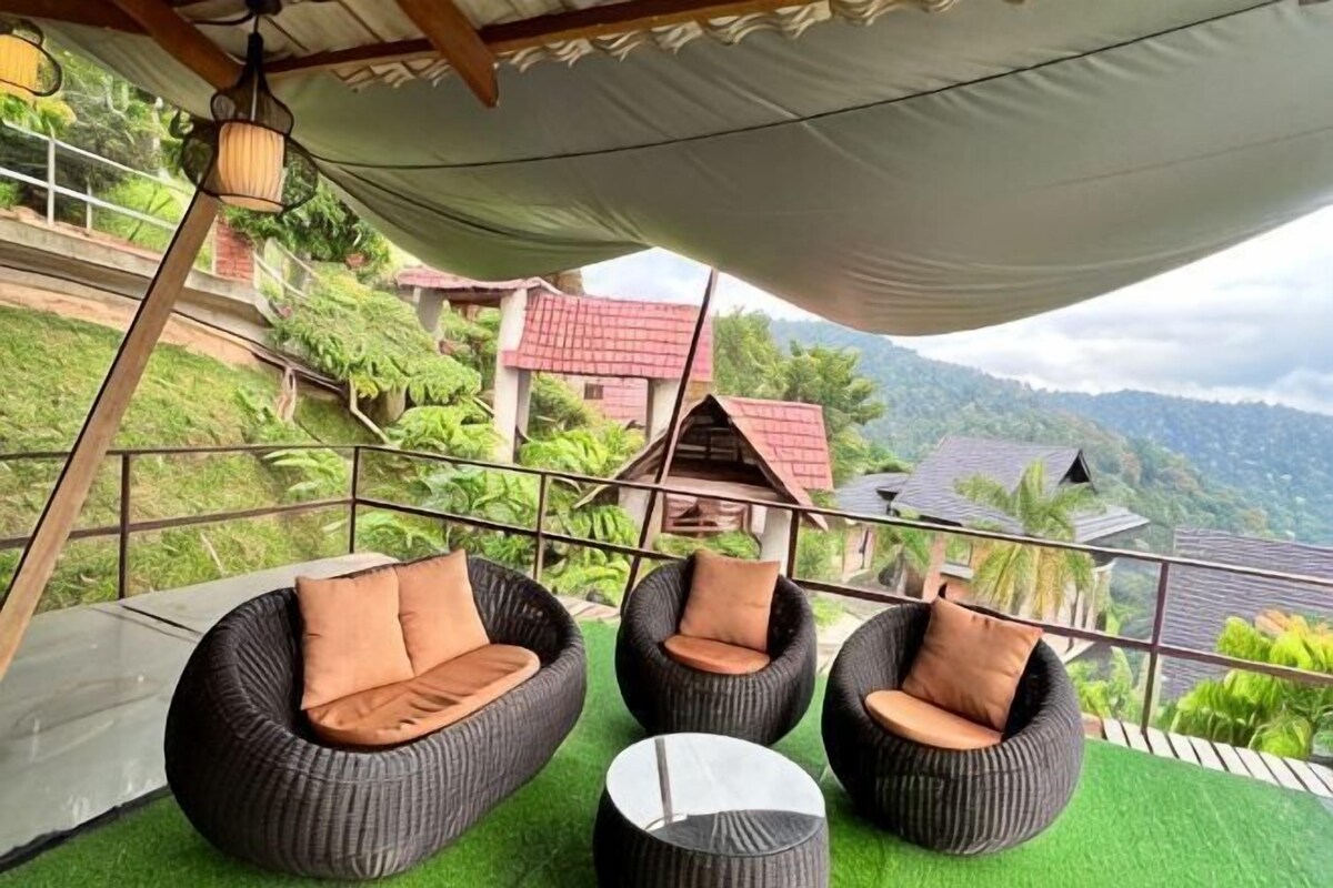 Outdoor seating with cushions, a small round table, and a view of a hillside with buildings.