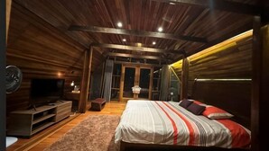 A bedroom with a wooden ceiling, a bed with striped bedding, a TV, and a small table. - Sankara Garden (Seremban)