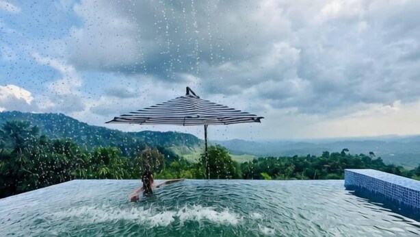 A person in a pool with a striped umbrella, surrounded by lush greenery and a cloudy sky. - Sankara Garden (Seremban)