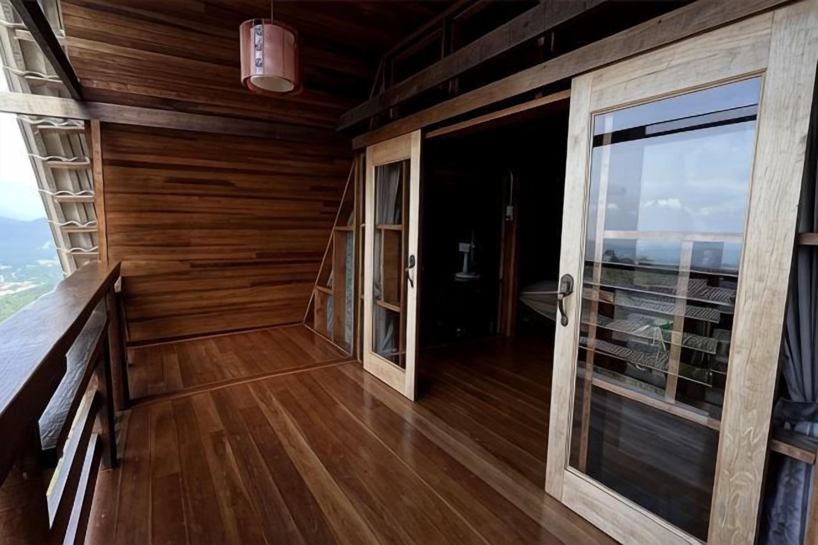 A wooden balcony with a glass door leading to a room.