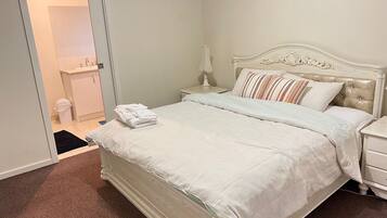 A neatly made bed with a white headboard and footboard, a bedside table with a lamp, and a bathroom visible through an open door.