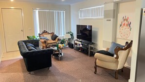 A living room with a black sofa, a beige armchair, a wooden coffee table, a TV on a stand, and a painting on the wall. - Quiet Abode with convenience. 3 Large bedrooms, whole house. (Melton South)