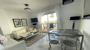 Una sala de estar moderna con una mesa de centro de vidrio, un sofá blanco y una zona de comedor con una mesa y sillas de vidrio.