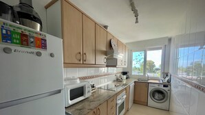 Una cocina moderna con armarios de madera, un refrigerador blanco, un microondas, un lavavajillas y una lavadora.