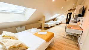 Un dormitorio con tragaluz, una cama con almohadas, un escritorio con silla y una kitchenette al fondo.