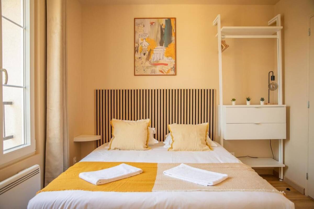 A hotel room with a bed, a bedside table, a wall-mounted artwork, and a white wardrobe.