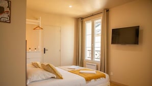 Un dormitorio con cama, televisión, ventana con cortinas y puerta.