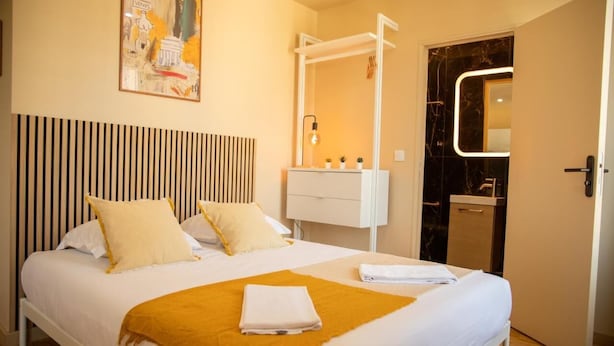 Habitación de hotel con una cama, una mesita de noche con lámpara, un espejo y una puerta al baño.