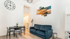 A modern living room with a dining table, blue sofa, and artwork on the wall.